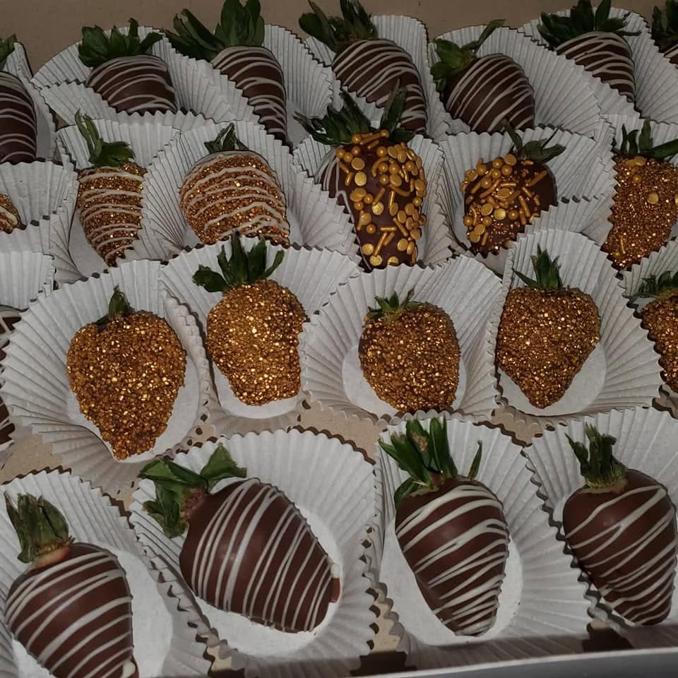 Chocolate-covered strawberries with white chocolate drizzles and gold sprinkles in white paper liners.