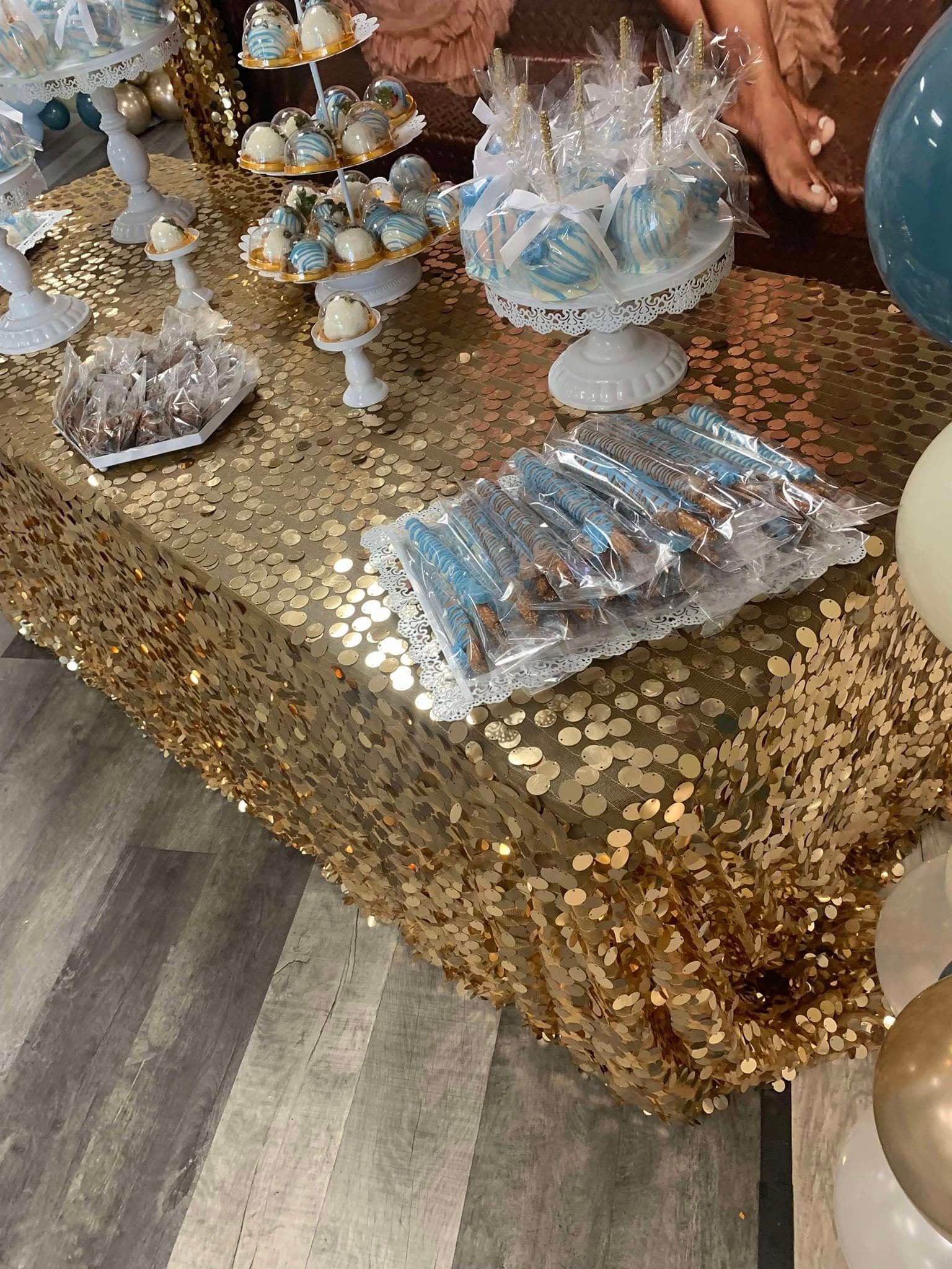 Gold sequin table with blue and white chocolate-covered pretzels, cake pops, and candied apples.