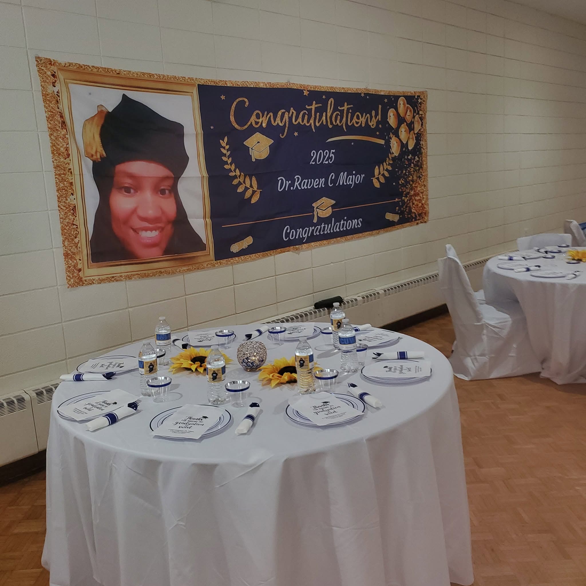 Graduation party setup with a banner for Dr. Raven C Major and decorated round tables.
