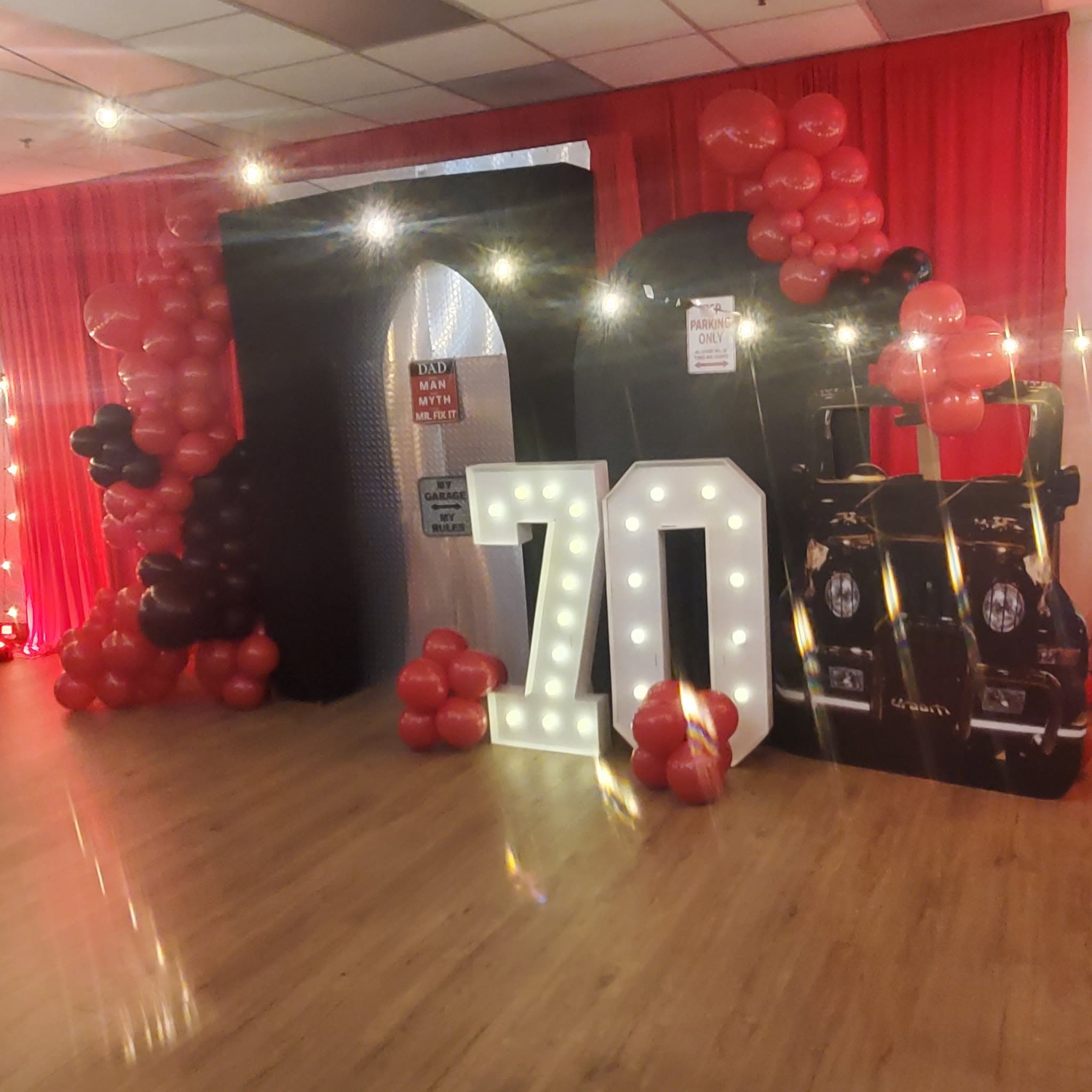 Large lit-up marquee numbers 70 with red and black balloons and car-themed party decorations.