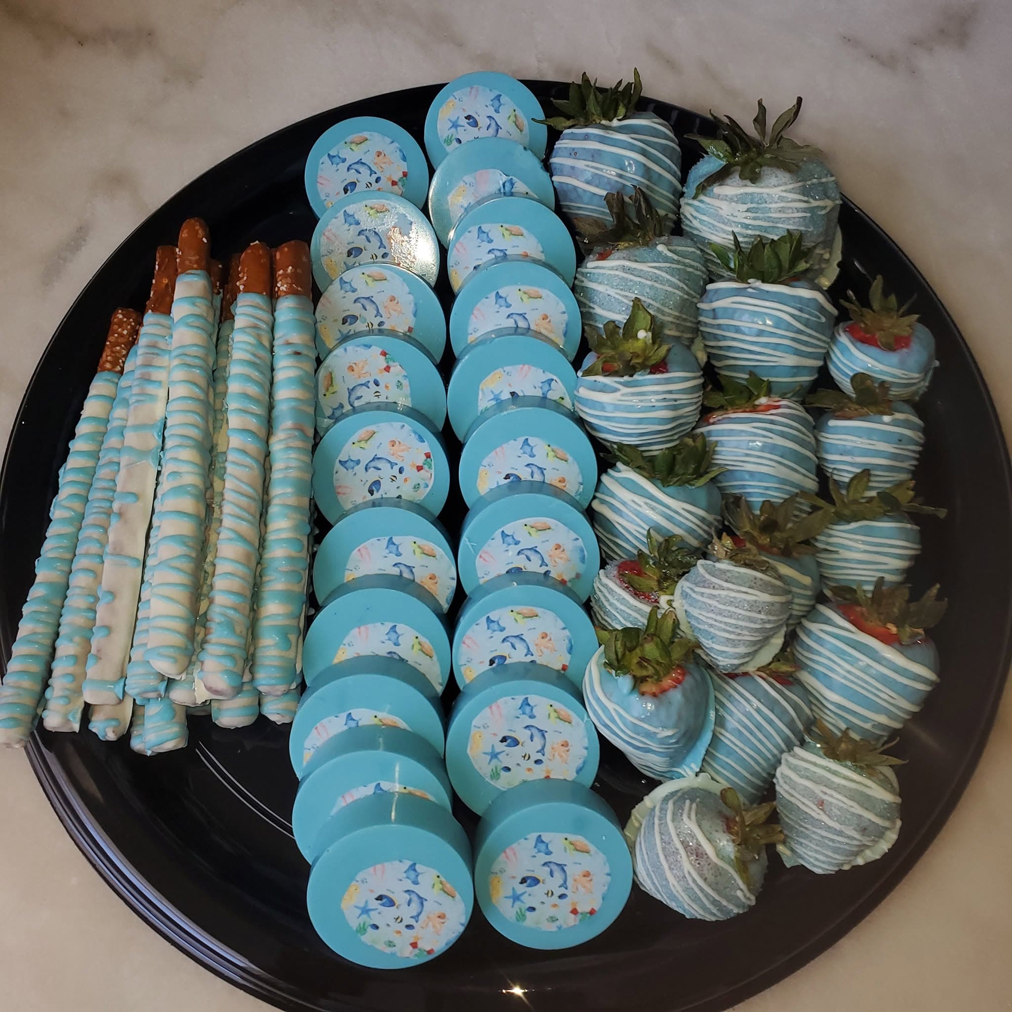 Ocean-themed dessert platter with blue chocolate-covered pretzels, sea creature cookies, and drizzled strawberries.