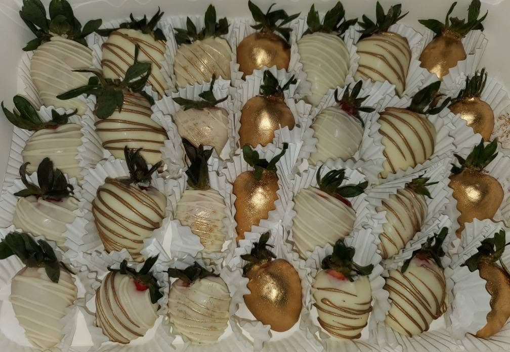 White chocolate-covered strawberries with gold drizzle and solid gold coating arranged in a box.