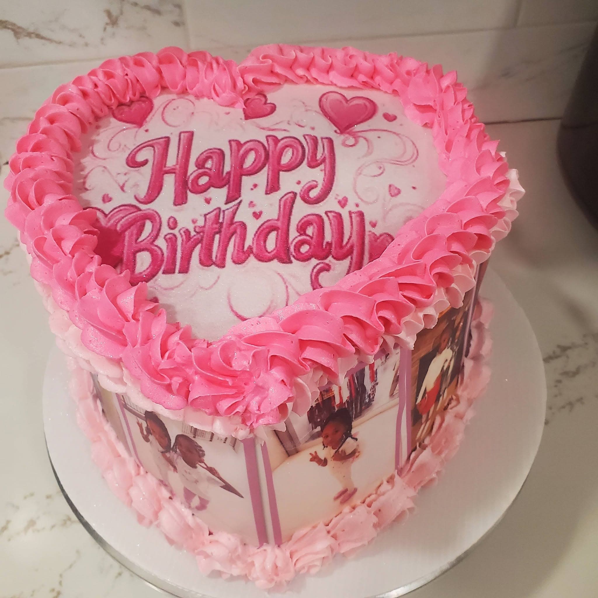 Heart-shaped pink cake with "Happy Birthday" text and printed photos of a child on sides.