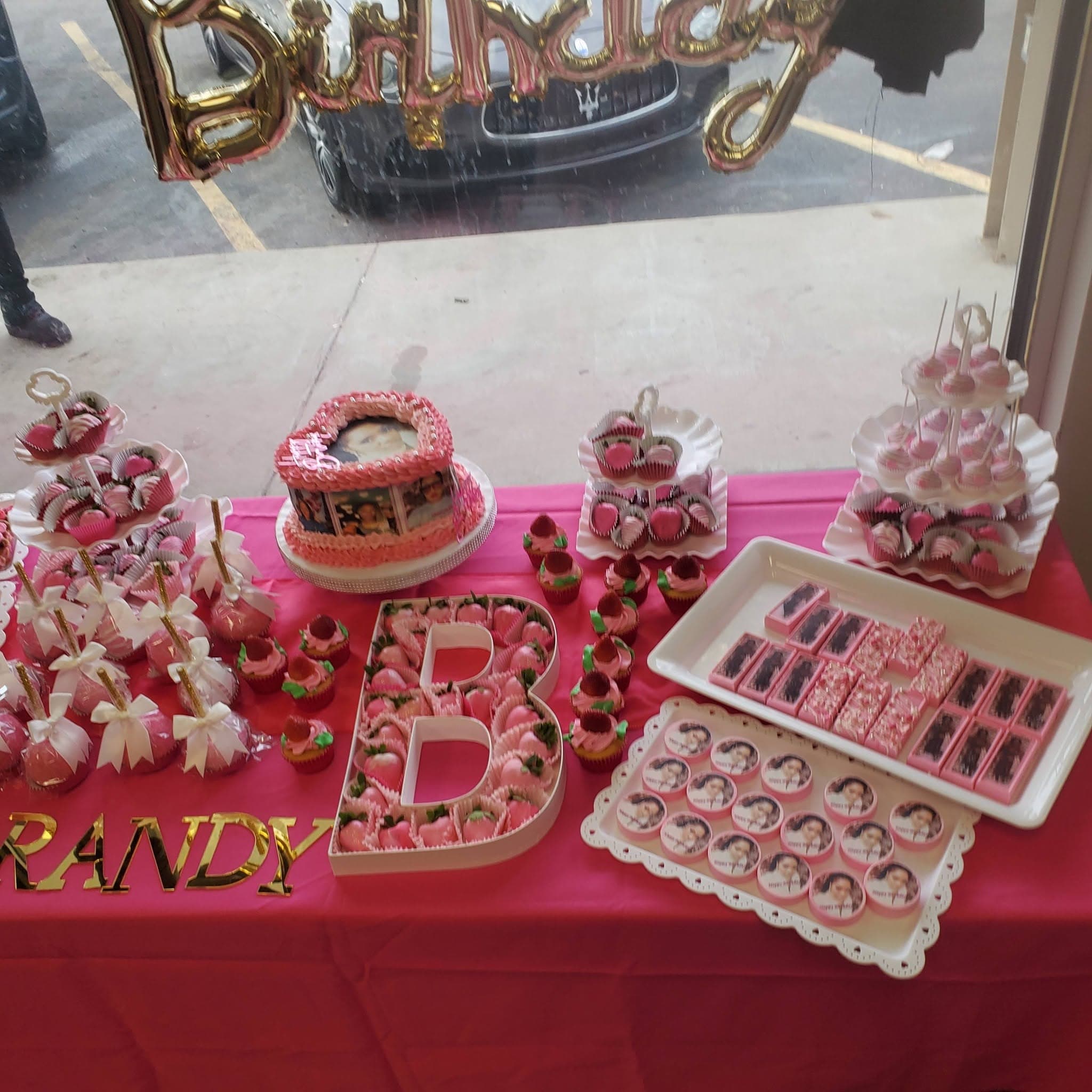 Pink birthday dessert table with a heart cake, photo treats, and strawberry-filled letter B.