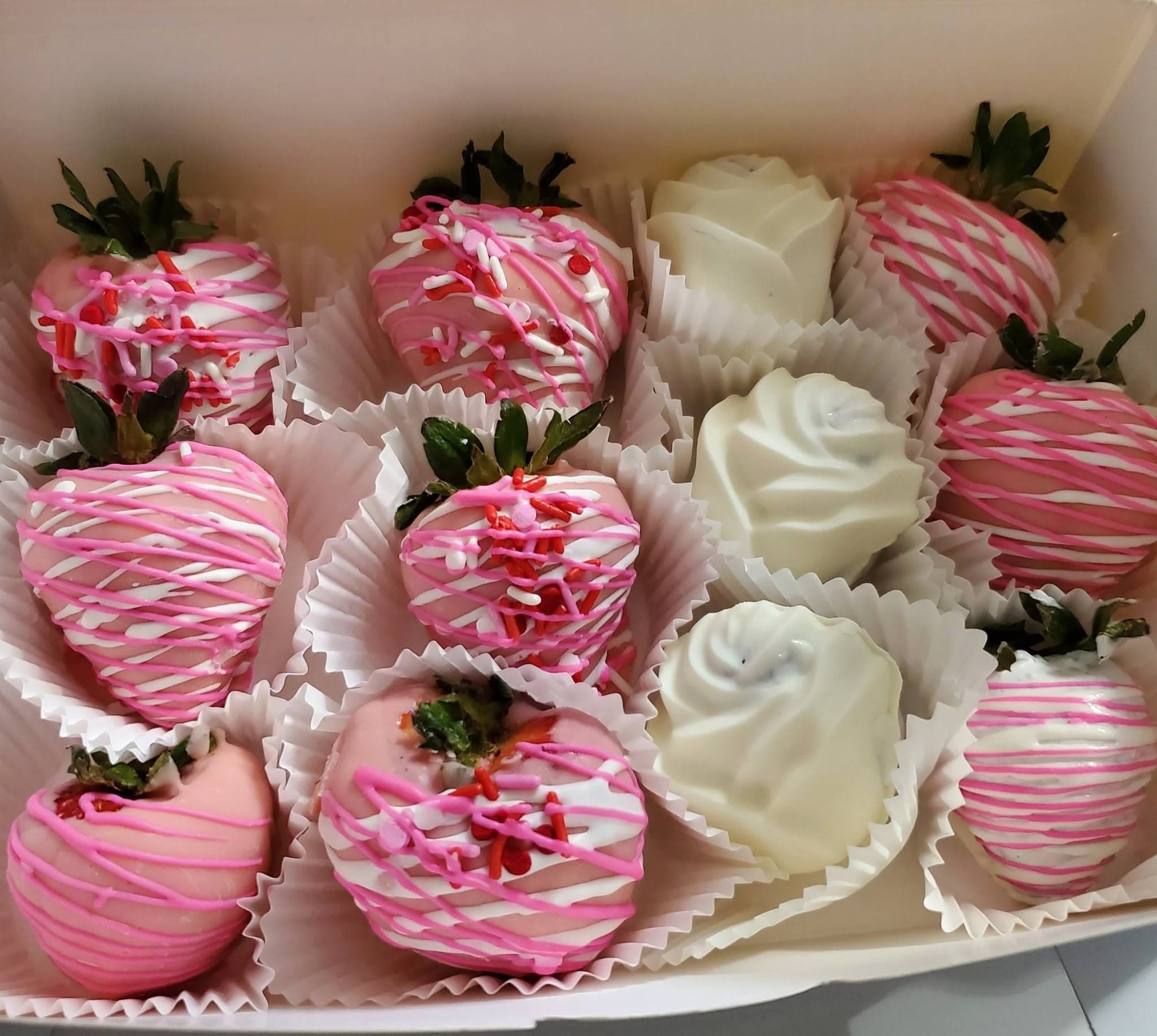 Pink chocolate-covered strawberries with drizzles and sprinkles, and white chocolate roses in a box.