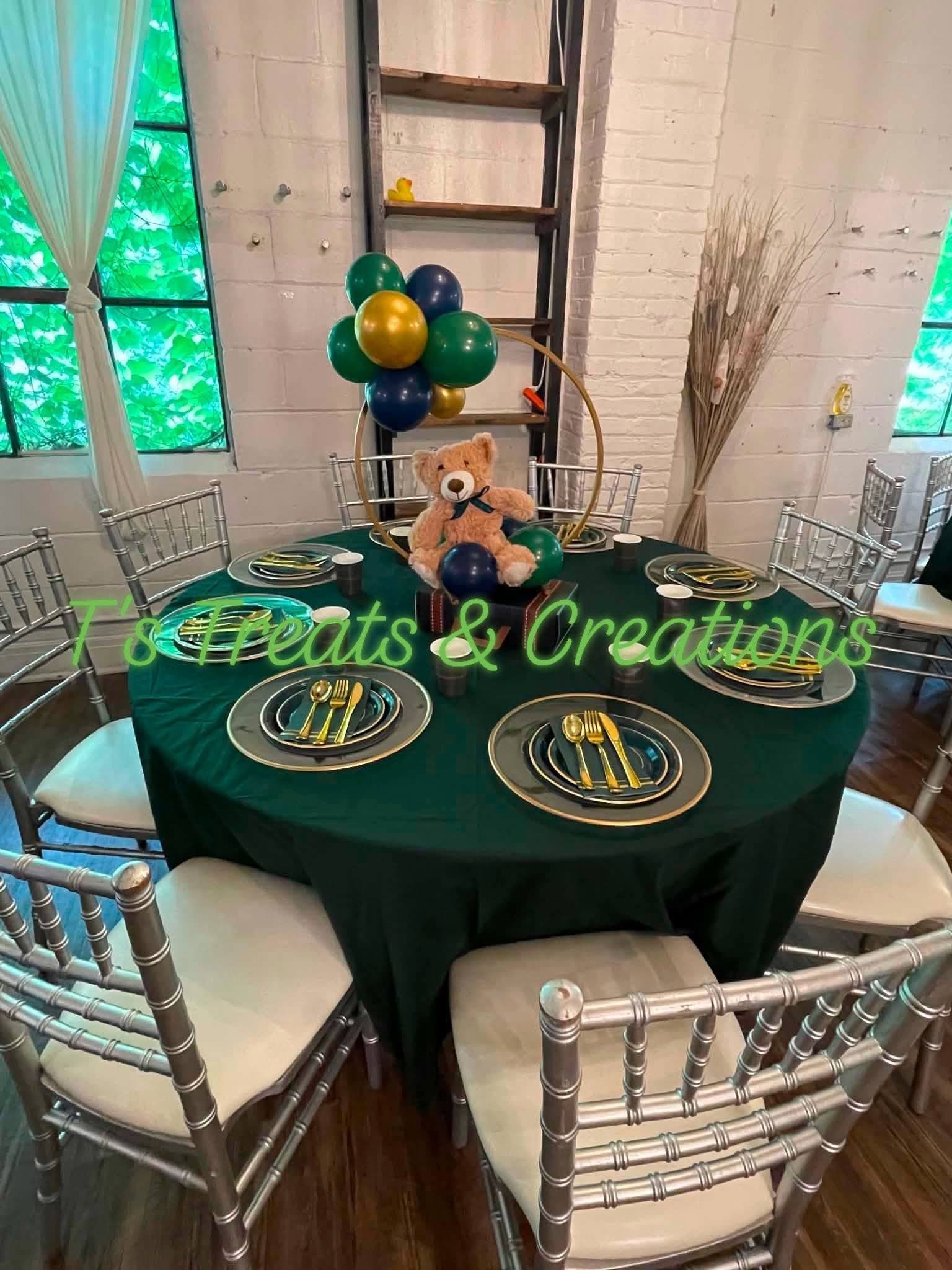 Elegant green table setting with gold-rimmed plates and a teddy bear balloon centerpiece.