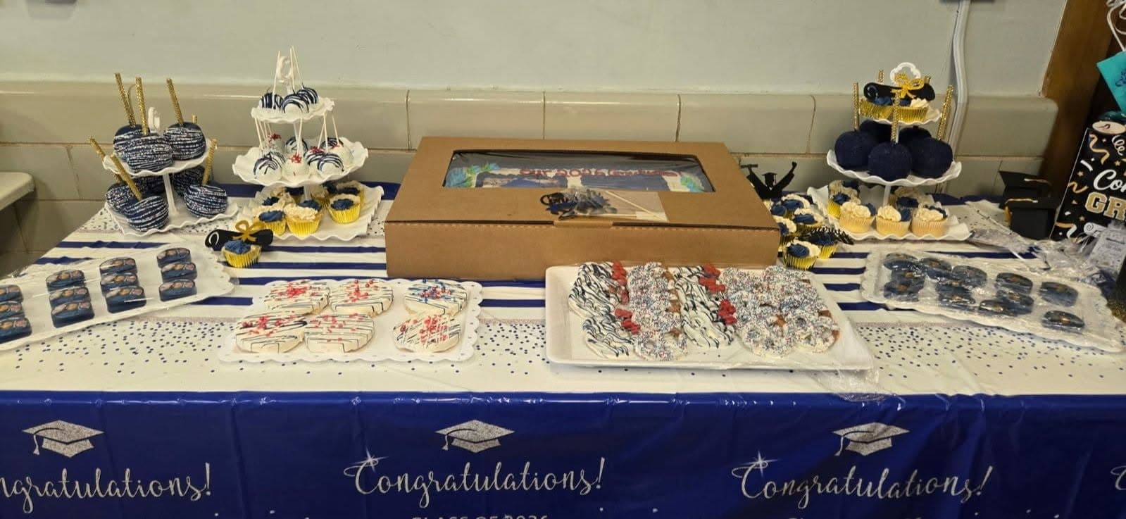 Graduation dessert spread with blue and white cupcakes, cake pops, cookies, and chocolate-covered pretzels.