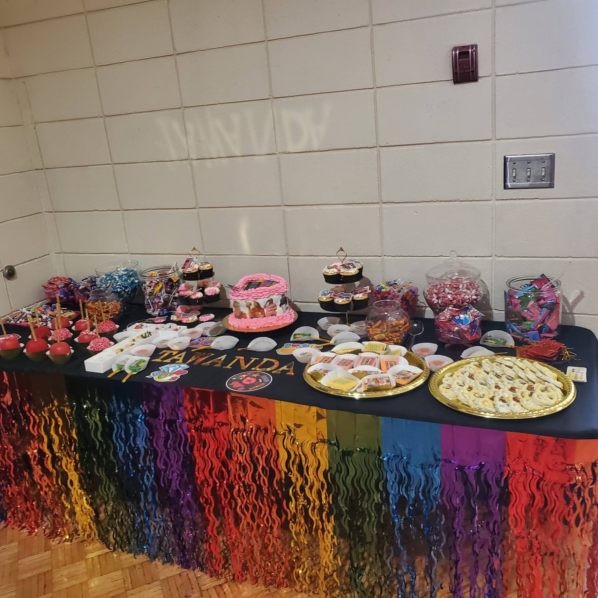 Festive dessert table with rainbow fringe, pink cake, and candy jars for a Tawanda celebration.