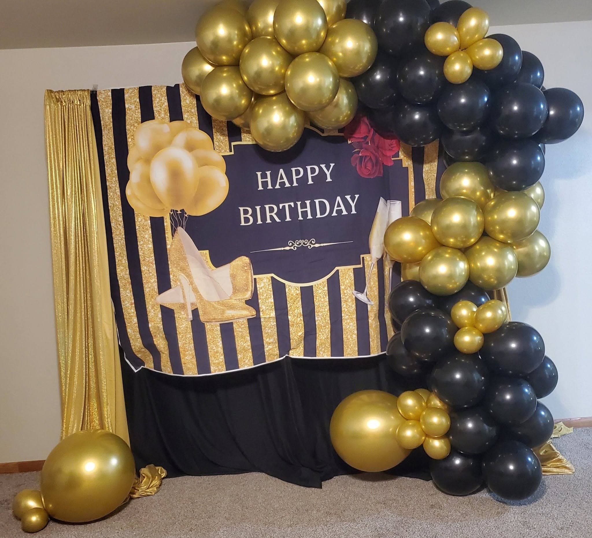 Glamorous black and gold birthday setup with a balloon arch and Happy Birthday backdrop.