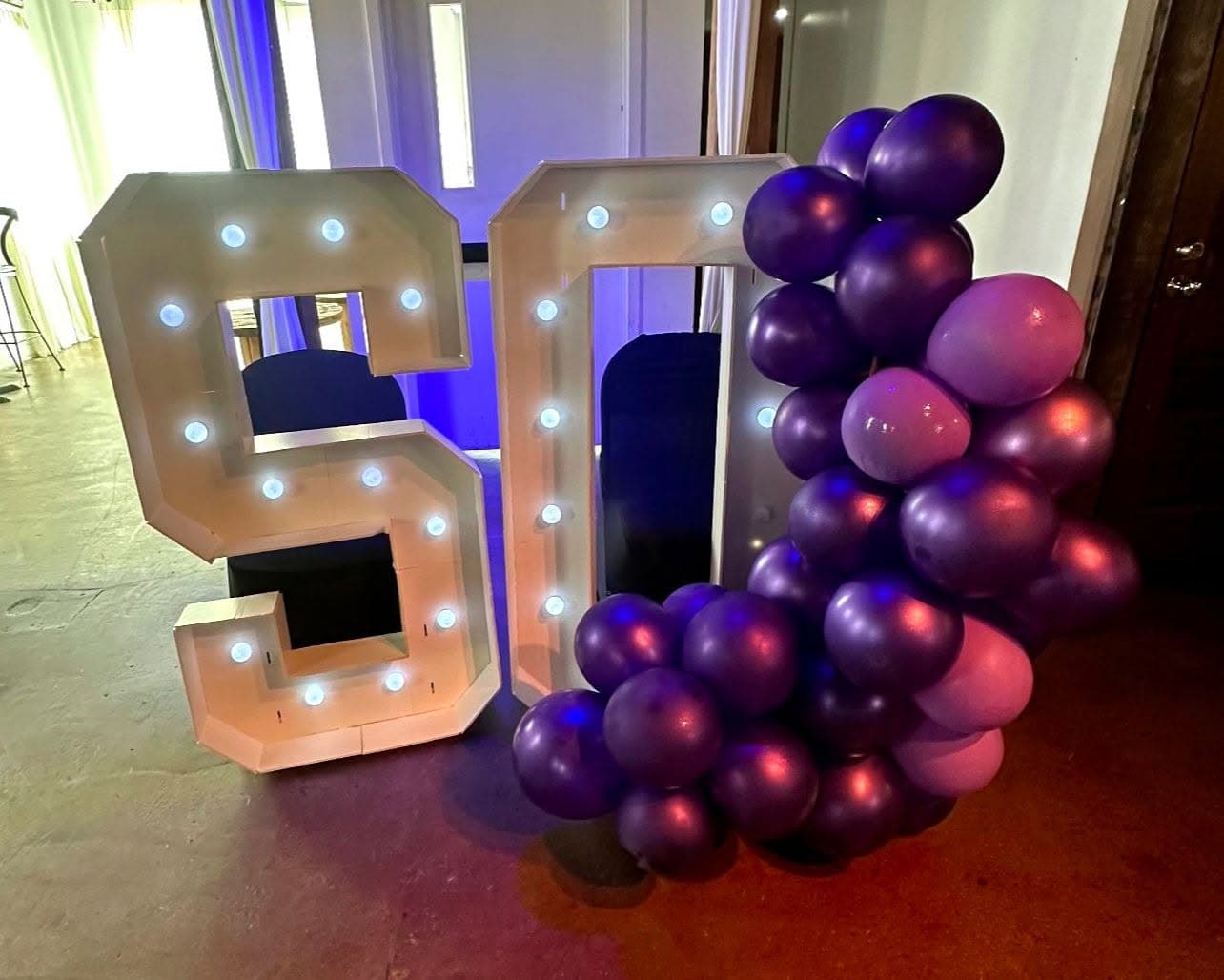 Large white light-up numbers fifty decorated with a cluster of purple and pink balloons.