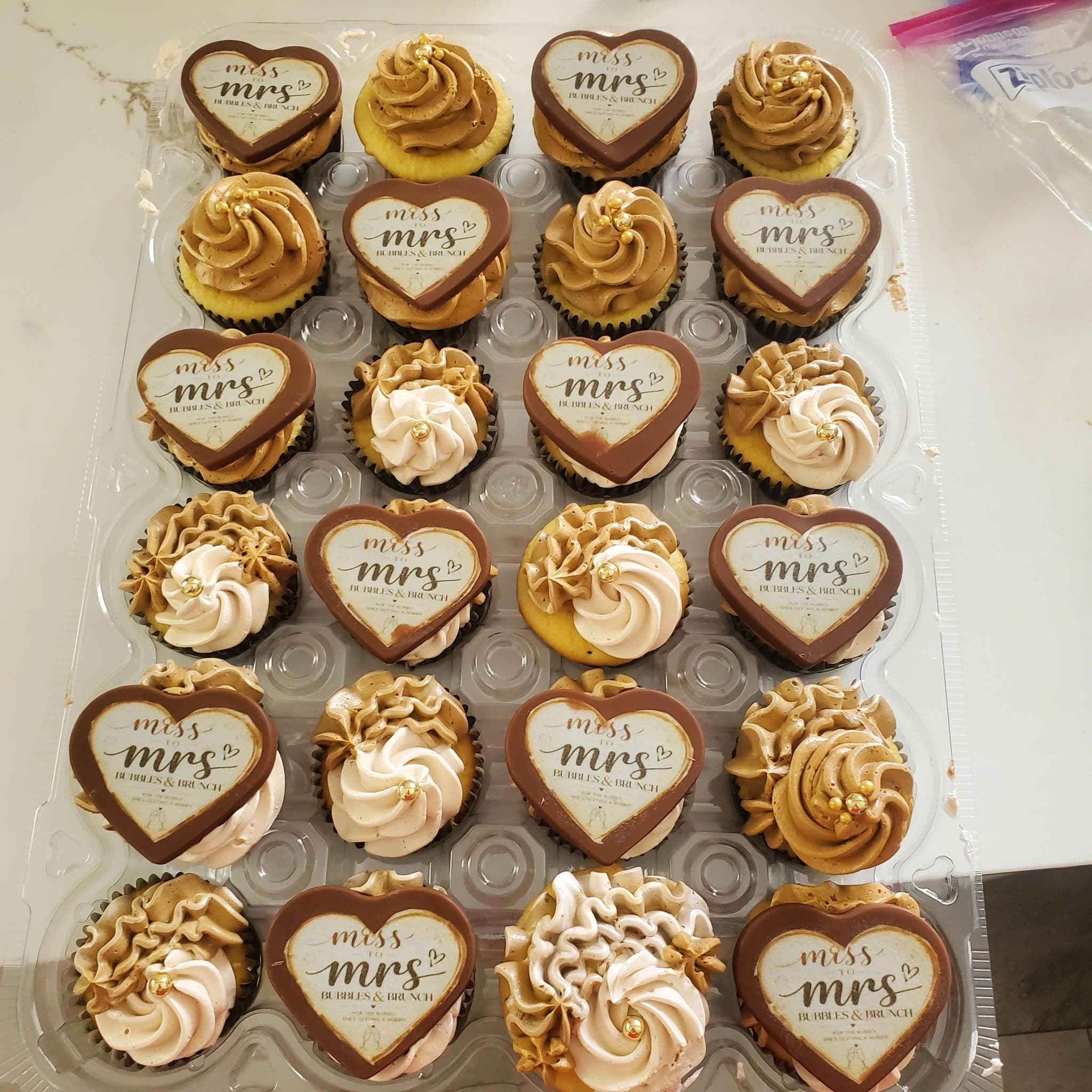 Cupcakes with tan frosting, gold pearls, and heart-shaped "Miss to Mrs Bubbles & Brunch" toppers.