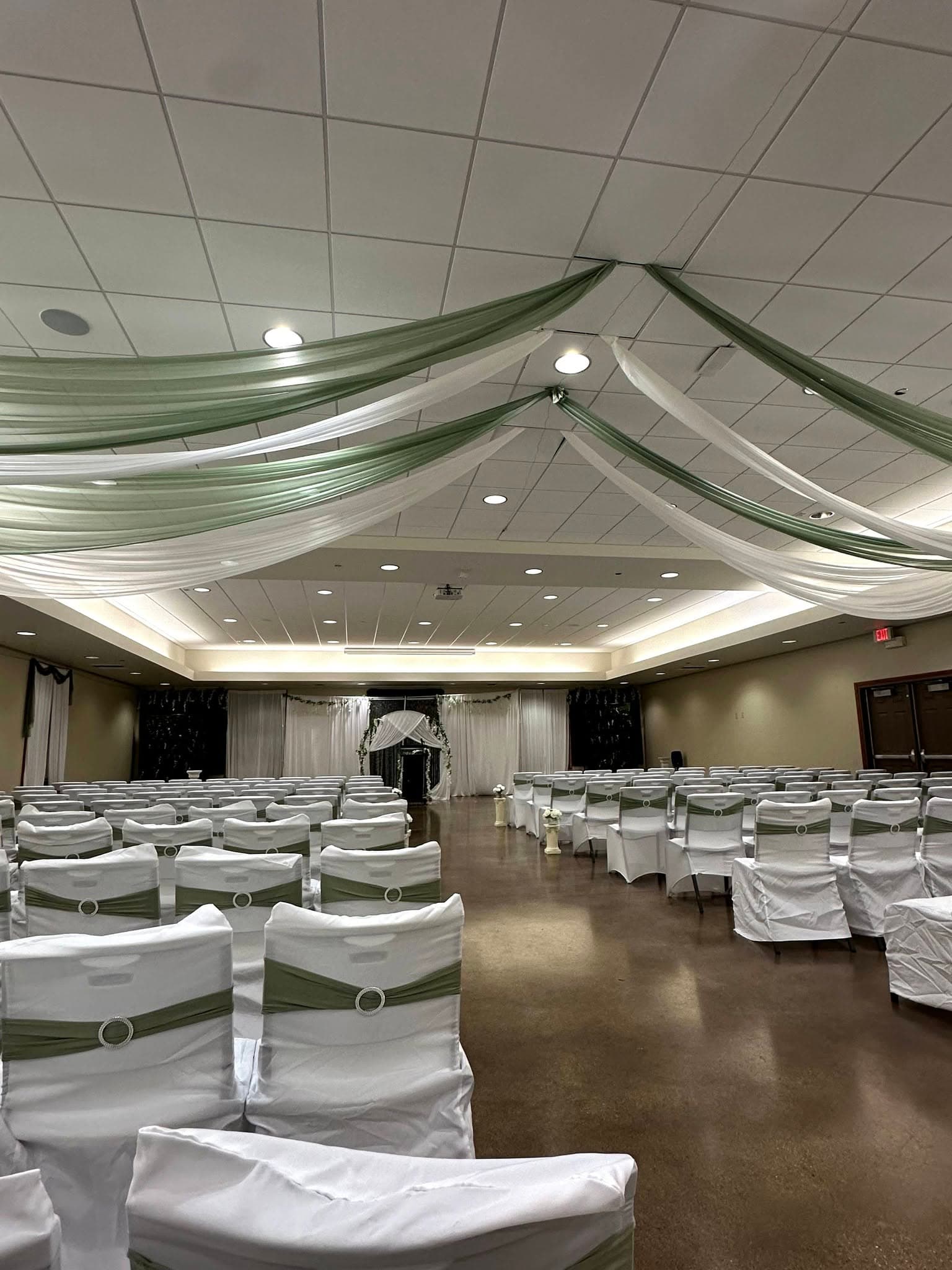 Rows of white chairs with green sashes under elegant green and white ceiling fabric drapes.