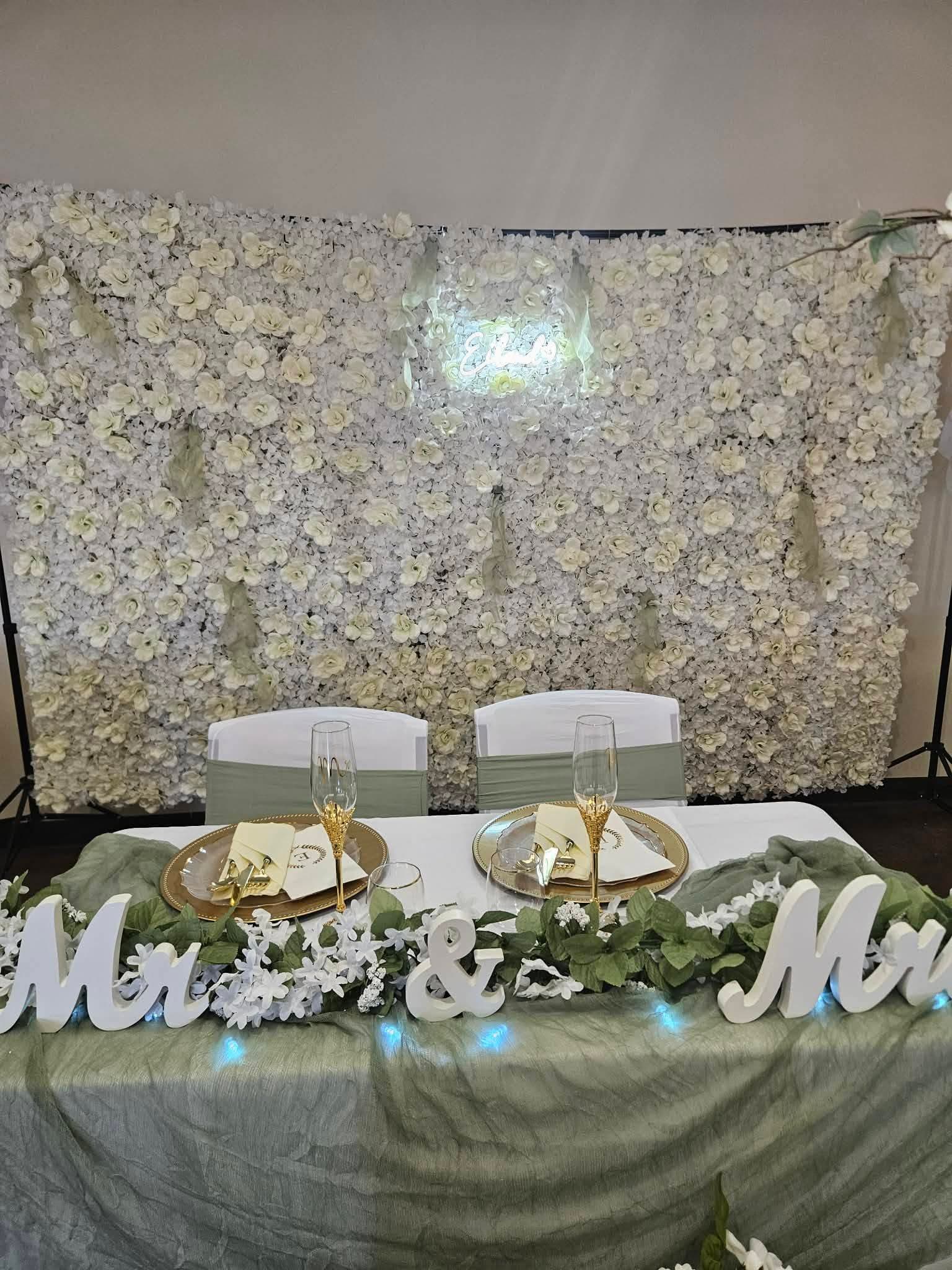 Sweetheart table for two grooms with white flower wall and 'Mr & Mr' sign.