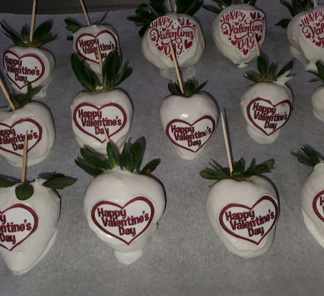 White chocolate-covered strawberries decorated with red "Happy Valentine's Day" hearts on a tray.