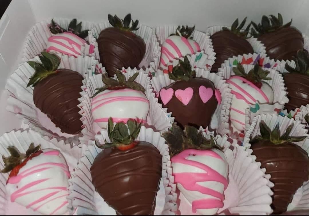Dark and white chocolate-covered strawberries with pink drizzles and hearts in a white box.