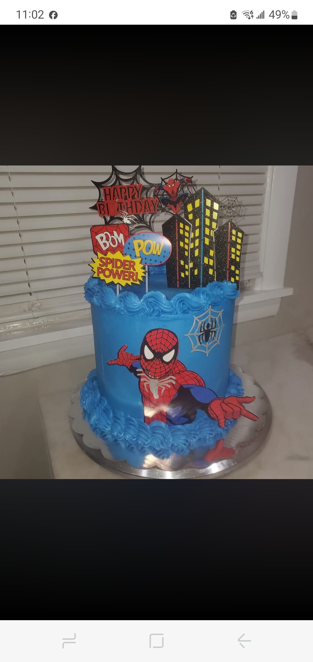 Blue Spider-Man birthday cake featuring city skyline toppers, comic bubbles, and a large character cutout.