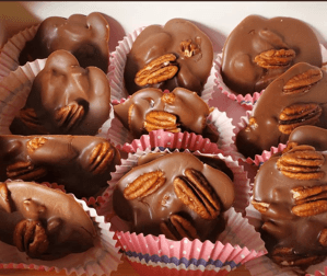 Milk chocolate pecan clusters topped with whole pecans in pink and white paper liners.
