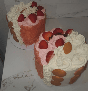 Two round cakes decorated with pink and white frosting, fresh strawberries, and vanilla wafer cookies.