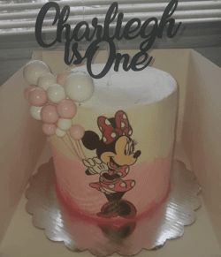 Pink and white ombre cake featuring Minnie Mouse and a "Charliegh is One" topper.
