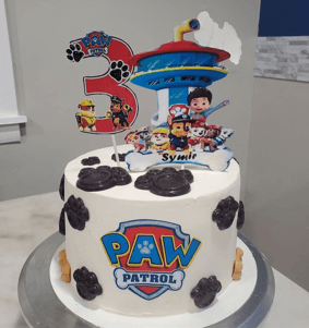 White Paw Patrol cake with black paw prints and character toppers for a third birthday.